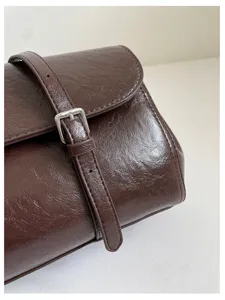 Close-up detail of dark brown shiny leather shoulder bag with buckle strap texture.