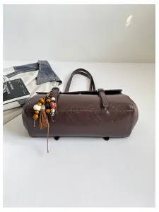 Detail view of dark brown leather shoulder bag with buckle and beaded tassel charm.