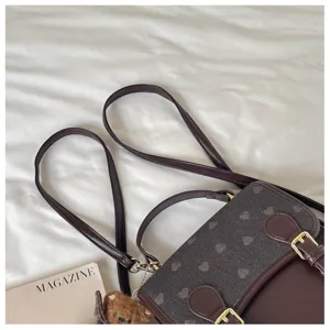 Detail view of the dark brown heart patterned backpack showing straps, handle and front buckle.