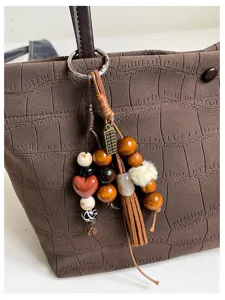 Dettaglio ravvicinato di una elegante borsa tote marrone con ciondolo nappa e perline.
