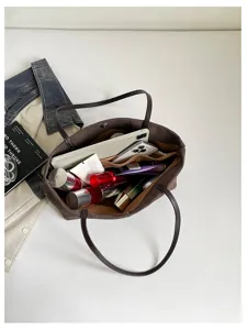Vista dettagliata dell'interno della borsa tote marrone effetto coccodrillo piena di cosmetici.