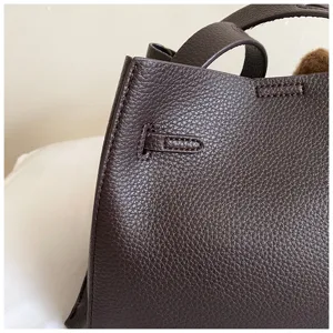 Brown textured leather handbag detail shot, showing fine craftsmanship and side buckle design.
