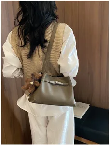 Detailed view of women's leather shoulder bag with chic metal lock and cute bear pendant.