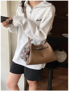 Detail view of a stylish brown leather crossbody bag with metal lock closure and cute charm.