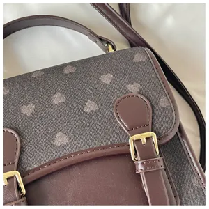 Close-up detail of brown heart pattern satchel bag featuring metal buckle and faux leather.