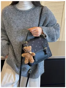 Detailed view of the black retro shoulder bag with cute teddy bear plush pendant in daily use.