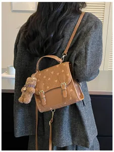 Detail view of the stylish brown fashion backpack with heart pattern and cute bear pendant.