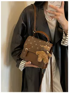 Detail view of a brown heart-pattern retro shoulder bag with cute bear pendant for autumn.