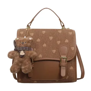 Chic brown heart print canvas backpack with cute plush bear pendant, stylish casual schoolbag.