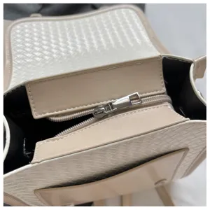 Detalle de mochila tejida elegante con textura de cuero beige y bolsillo con cremallera.