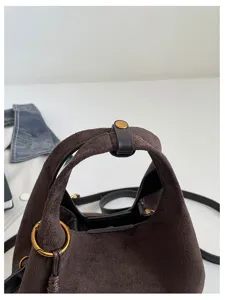 Gros plan détaillé de la poignée du sac à main en suède marron, avec texture et anneau métal.