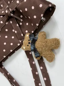Close-up detail of stylish brown polka dot tote bag featuring a cute fluffy bear charm.