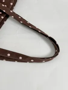 Brown polka dot tote bag handle detail showing soft suede fabric and neat white stitching lines.