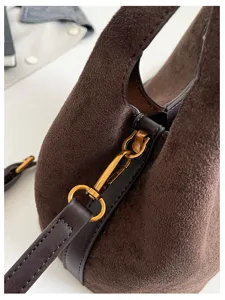 Détail de sac hobo en daim marron, gros plan sur la quincaillerie élégante du sac.