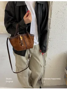 Detail shot of a stylish brown suede patchwork bucket bag with charm and crossbody strap.
