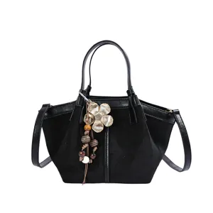 Black suede patchwork bucket bag featuring metal flower pendant and adjustable shoulder strap.