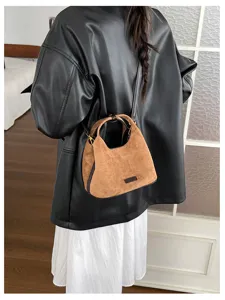 Détail de sac à main croissant en suédine marron avec poignées et bandoulière.