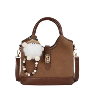 Close-up detail of the brown suede handbag featuring a metal lock and cute doll pendant.
