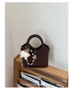 Dark brown minimalist bucket bag with plush charm and beaded strap for women daily use.