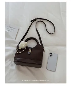 Detailed view of a chic retro brown bucket bag with pearl charm and shoulder strap on white.