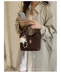 Close-up detail of dark brown leather bucket bag featuring metal lock and cute fluffy charm.