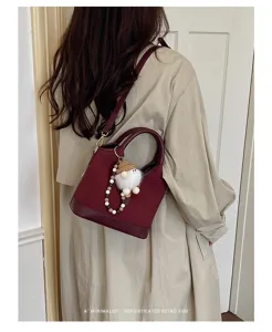Detailed view of stylish burgundy bucket bag with cute plush pendant and shoulder strap.