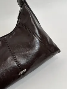Detailed view of the dark brown glossy underarm shoulder bag with metal zipper and clean stitching.