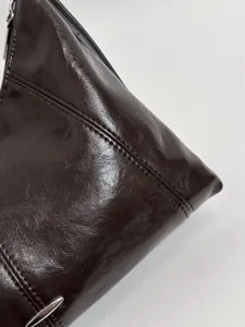 Detailed view of the glossy dark brown leather underarm bag, showing fine stitching texture.