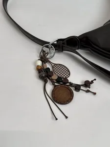 Detailed view of dark brown underarm shoulder bag featuring chic wooden bead and racket charms.
