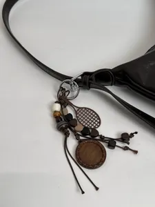 Detailed shot of dark brown minimalist leather underarm shoulder bag with cute wooden charm pendant.