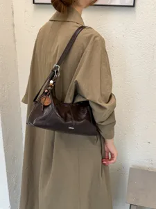 Detailed view of the brown leather hobo shoulder bag with beaded charm and trench coat.