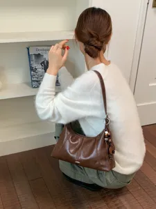 Brown leather underarm shoulder bag for women, stylish commuter dumpling bag with bead charm.