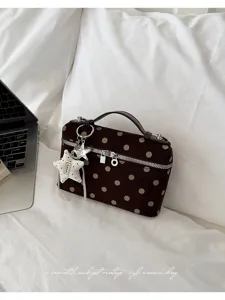 Detailed shot of brown velvet polka dot handbag with star keychain and golden zipper on white bed.