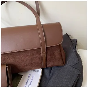 Detail shot of retro brown leather shoulder bag featuring suede panel and vertical strap.