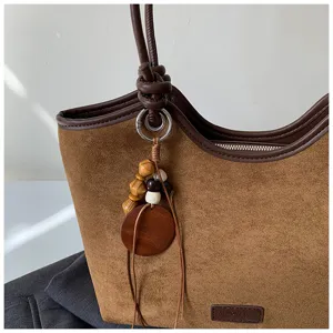 Detailed close-up of a stylish brown suede tote bag featuring a knotted handle and wooden bead.