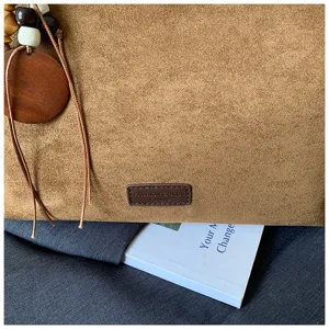 Close-up detail of brown suede handbag with wooden bead pendant and stylish leather label.