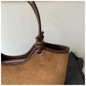 Brown suede tote bag detail showing the elegant knotted handle and metal ring craftsmanship.