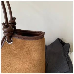 Brown suede bucket bag detail shot, showing exquisite leather trim and knotted handle.