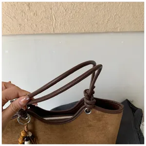 Brown suede tote bag detail featuring textured handle and decorative knotted string.