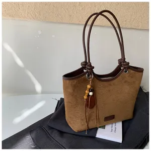 Detailed close-up shot of brown suede tote bag with elegant wooden bead tassel pendant.