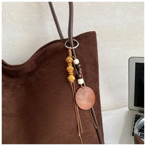 Brown suede shoulder bag detail showing the elegant wooden bead charm and textured fabric.