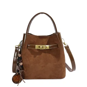 Brown suede bucket bag detail featuring metal turn-lock closure and rustic beaded charm.