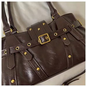 Detalle de bolso de hombro de cuero vintage marrón con hebillas metálicas y remaches estilo moto.