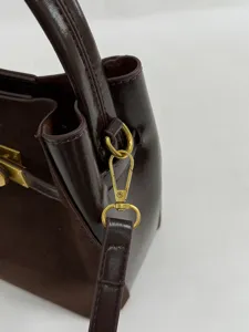Gedetailleerde close-up van donkerbruine lederen emmertas schouderriem metalen hardware.