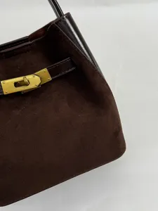 Detail van donkerbruine suède handtas met elegante goudkleurige draaisluiting.