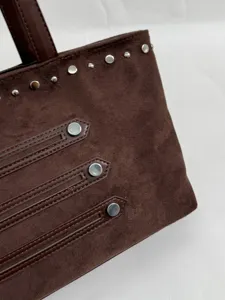 Close-up of brown suede tote bag featuring silver rivets and stylish strap details for women.