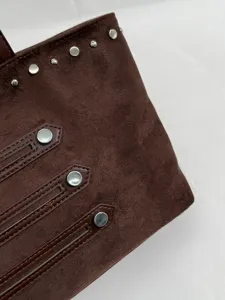 Brown suede handbag detail shot featuring metal studs and decorative leather straps.