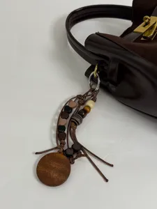Gedetailleerd uitzicht van donkerbruine lederen emmertas met houten kralen sleutelhanger