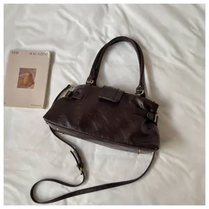 Detalle del bolso de hombro vintage marrón de cuero estilo moto retro con correas laterales y accesorios.