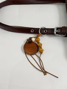 Close-up detail of women's brown leather handbag strap with wooden pendant and metal ring.